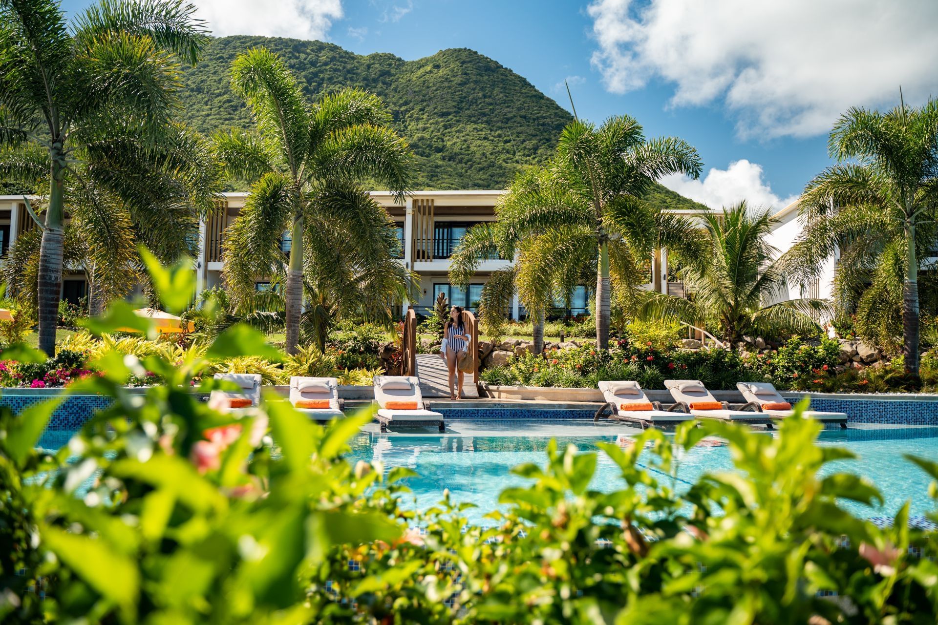 Couple strolling near a pool with palm trees and loungers, and green mountains in the background at Golden Rock Resort