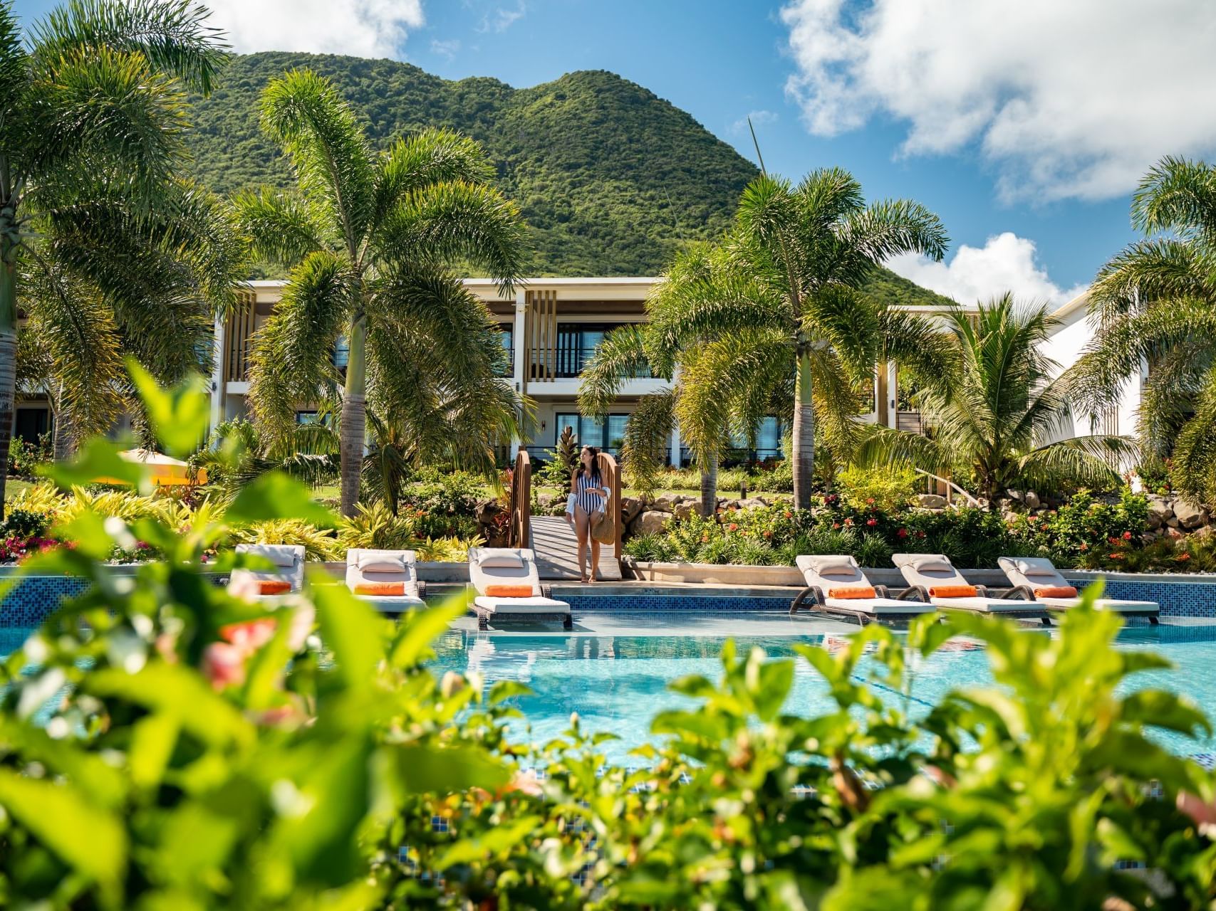 Couple strolling near a pool with palm trees and loungers, and green mountains in the background at Golden Rock Resort
