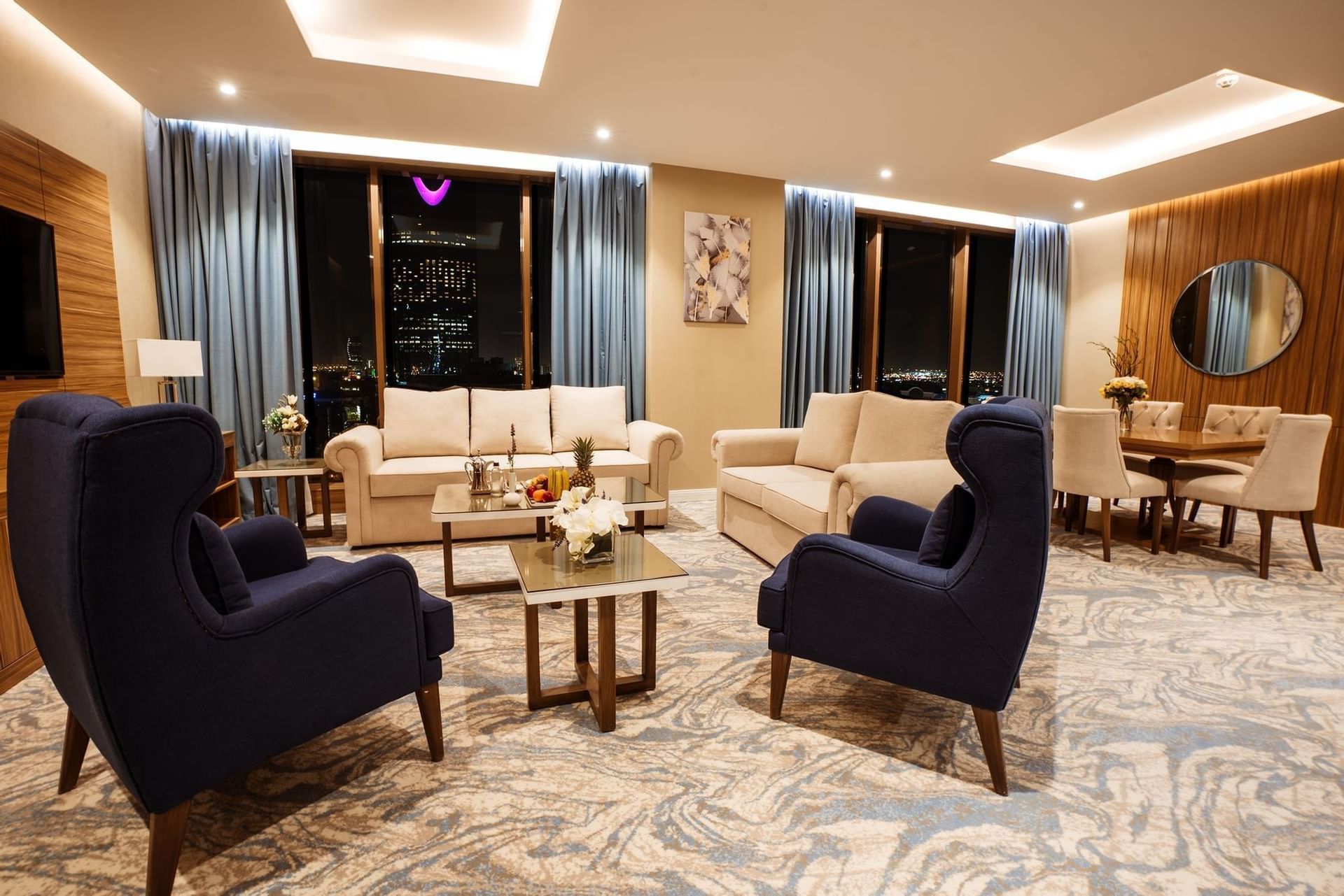 Elegant living area with sofas by a dining set under blue drapes at night in Royal Suite at Cantonal Hotel by Warwick Riyadh