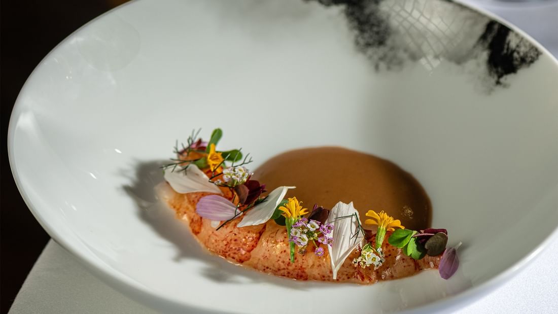 Lobster with sauce and garnished with edible flowers on a white plate at JEFF'S CELLAR, The Banjaran Hotsprings Retreat in Ipoh.