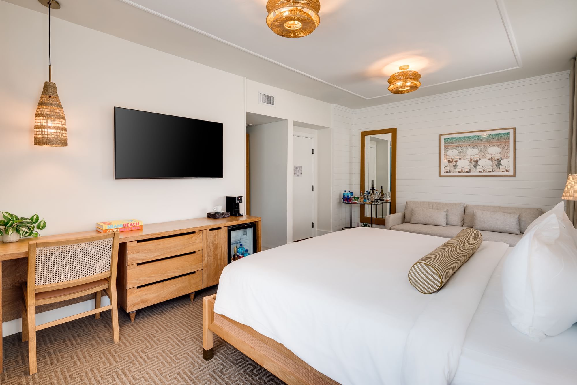 A hotel room with a king-sized bed, desk, TV, and mini-fridge.