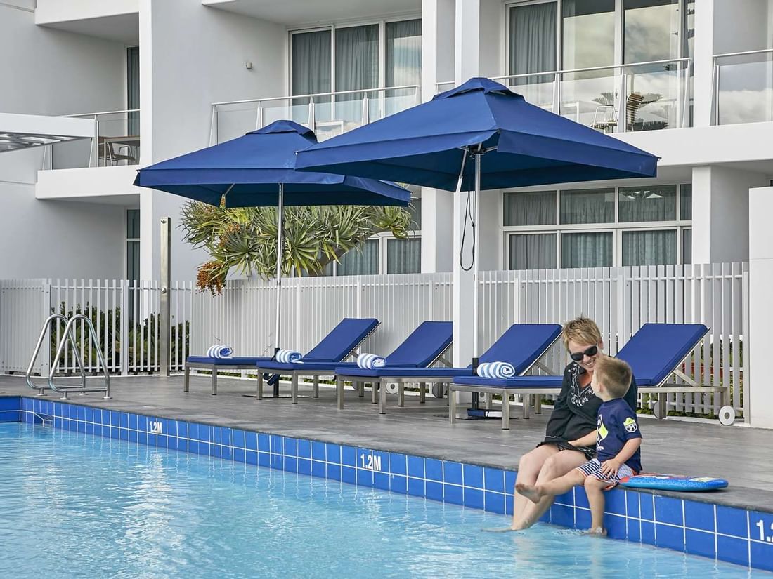 Woman and a child with their feet in the water sit at the pool's edge in The Sebel Mandurah