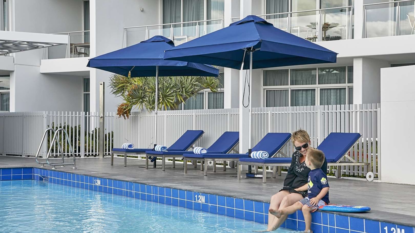 Woman and a child with their feet in the water sit at the pool's edge in The Sebel Mandurah