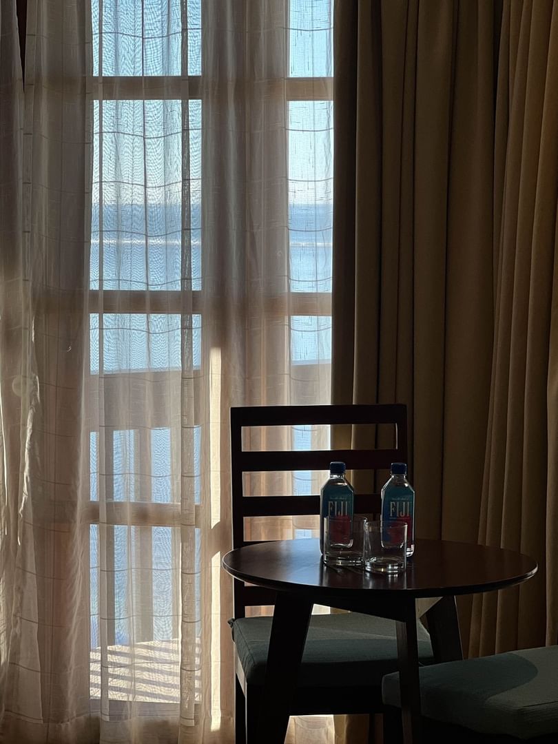 Wooden chairs by a round table with water bottles in front of sheer curtains at Warwick Hotels & Resorts