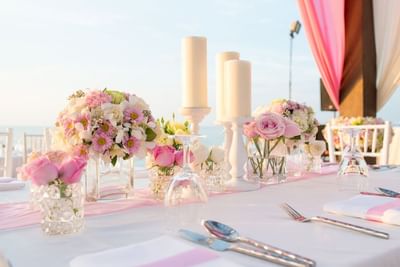 White candles with glasses set-up and floral centerpieces on a pink runner wedding table at The Abidah Hotel by Accra