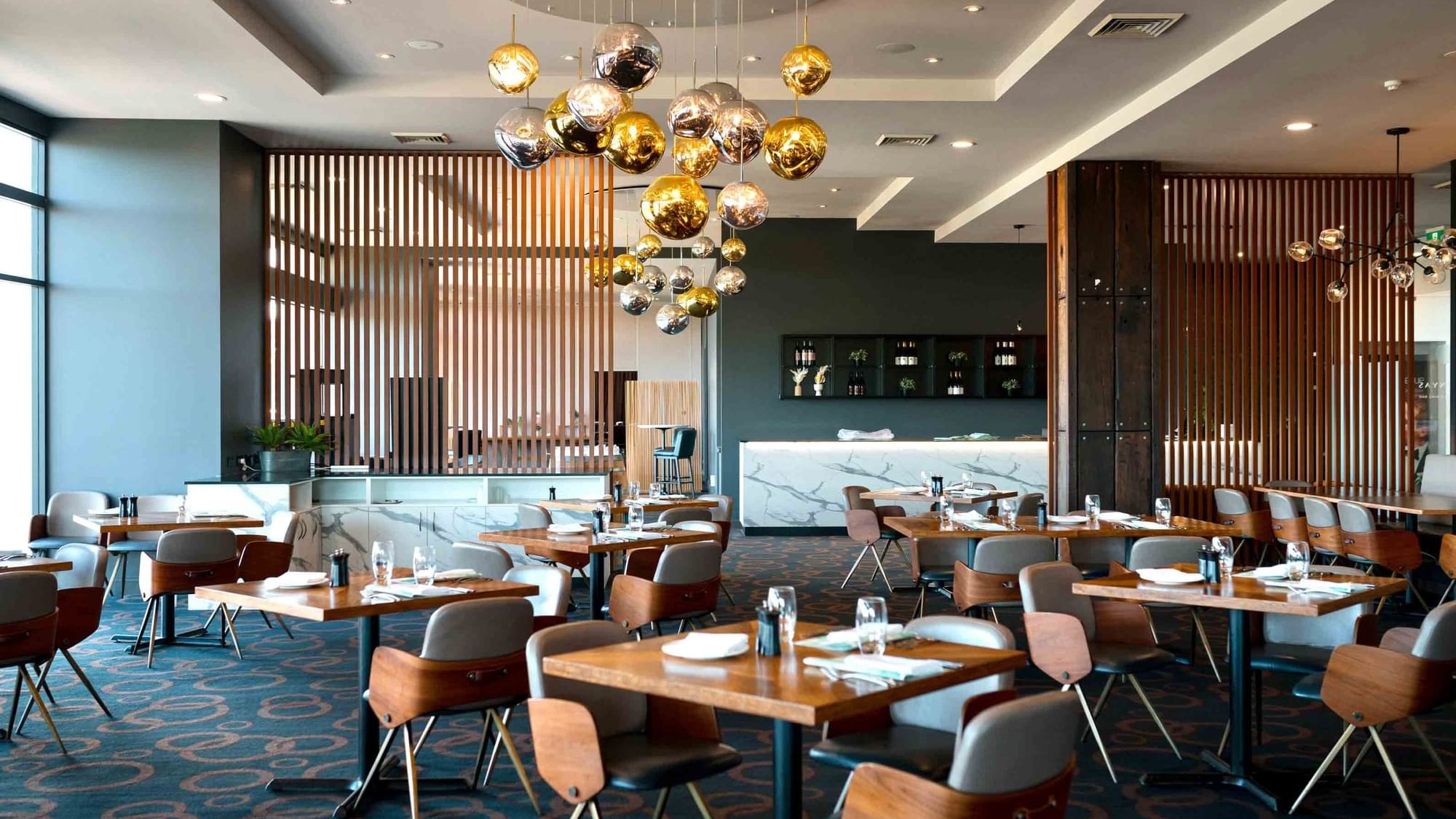 Karinyas Restaurant interior with stylish chairs and tables, pendant lights, and a bar area at Mercure Kooindah Waters