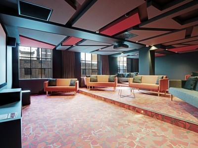 Modern communal lounge with colorful sofas, geometric ceiling panels, and large windows at UniLodge Auckland Central.