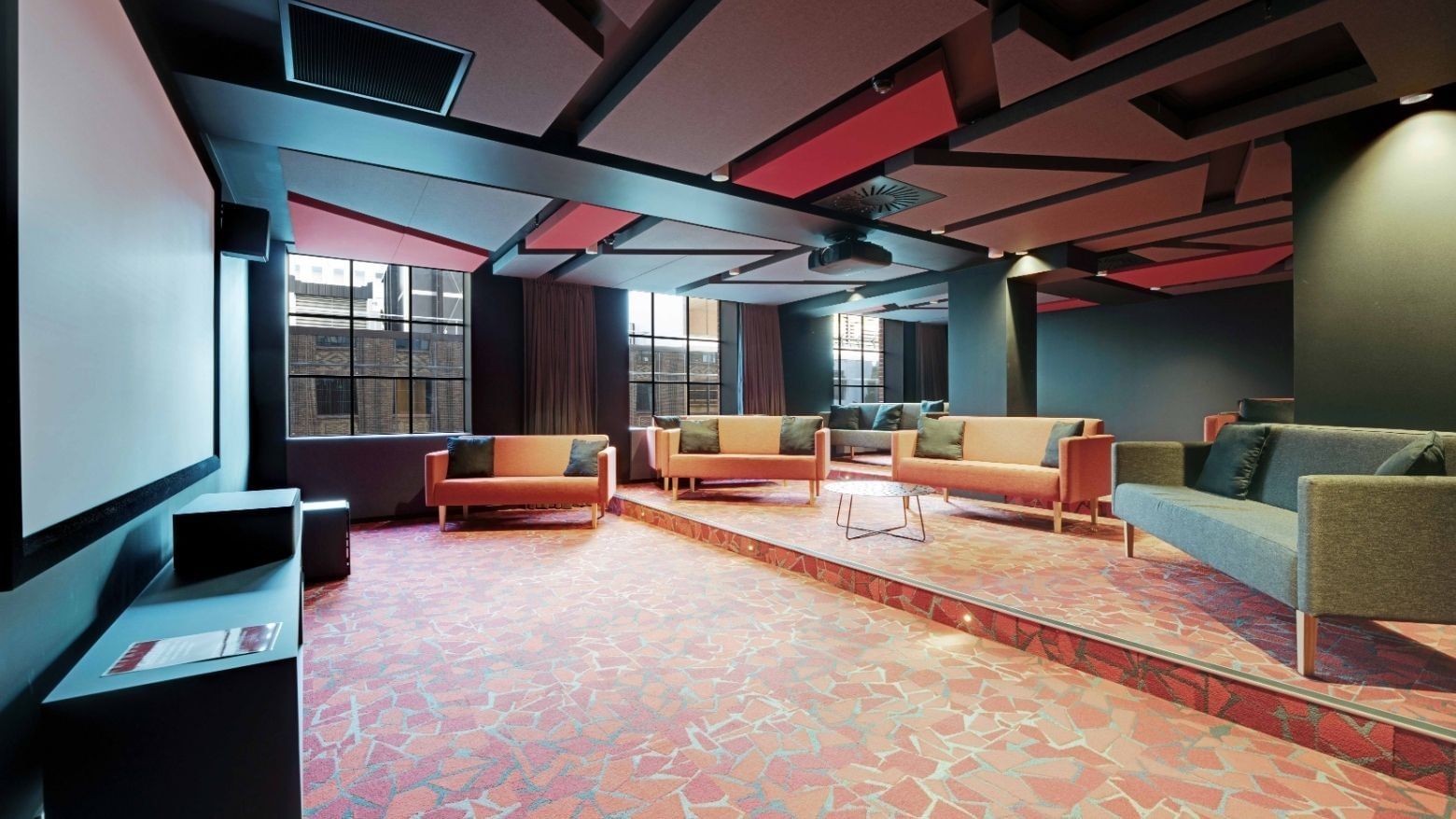 Modern communal lounge with colorful sofas, geometric ceiling panels, and large windows at UniLodge Auckland Central.