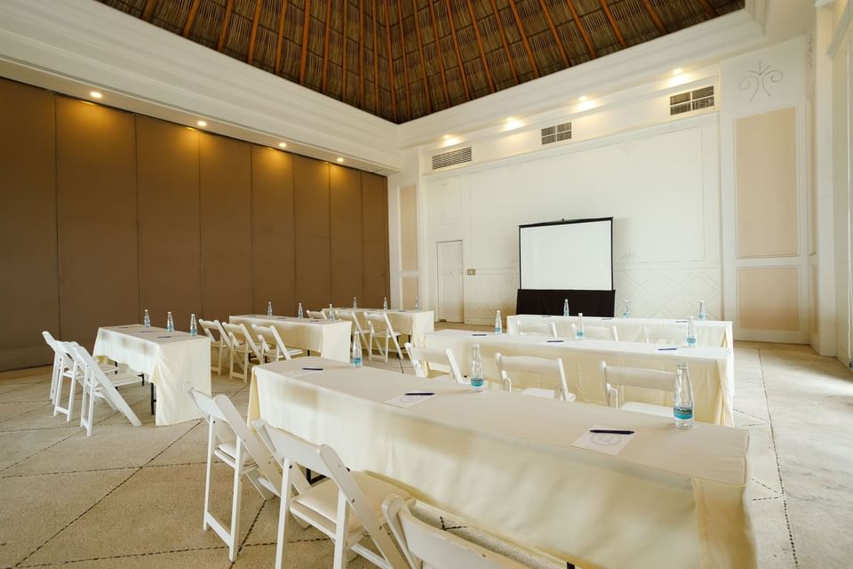 Ixtac Venue set up in classroom style with white tables, chairs, and a large screen at Quinta Real Acapulco