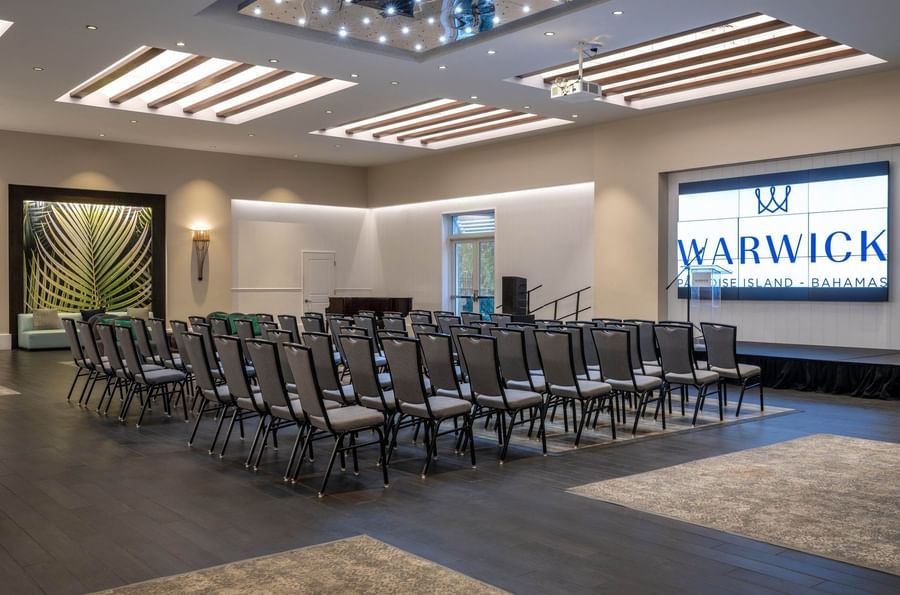 Rows of grey chairs by a large digital screen under a slatted ceiling in Meeting Room at Warwick Paradise Island Bahamas