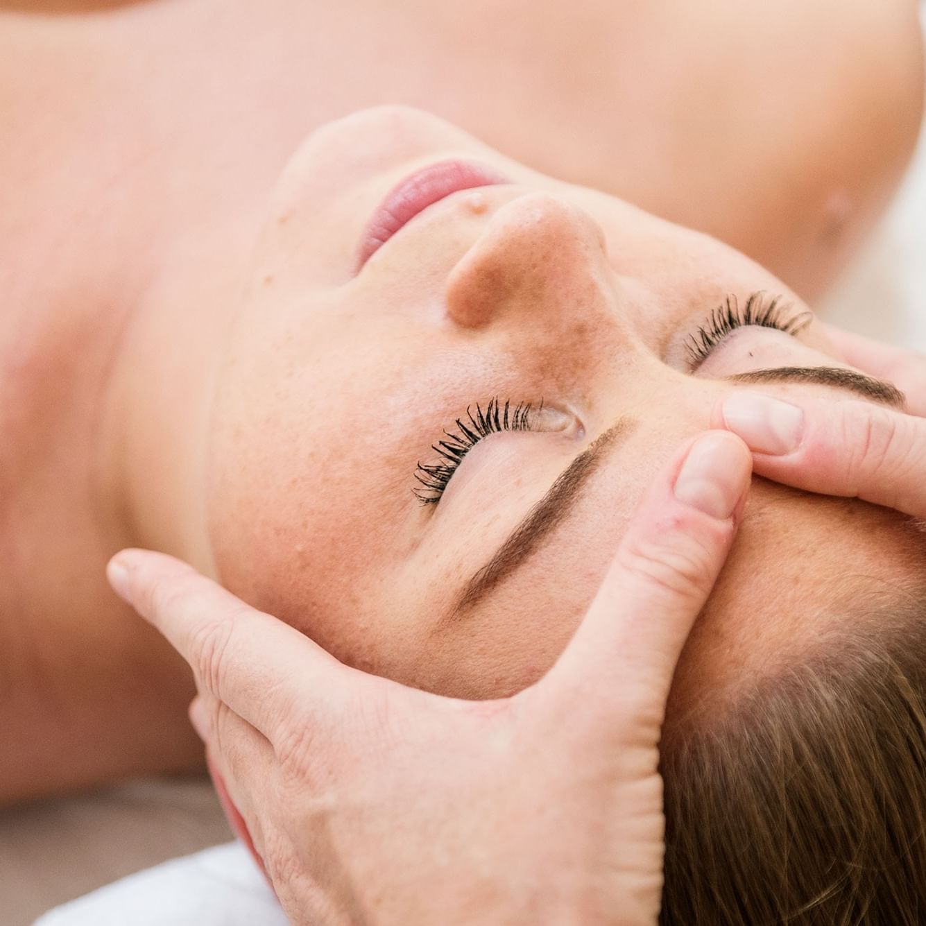 Woman receiving a facial massage with hands on her face and eyes closed.