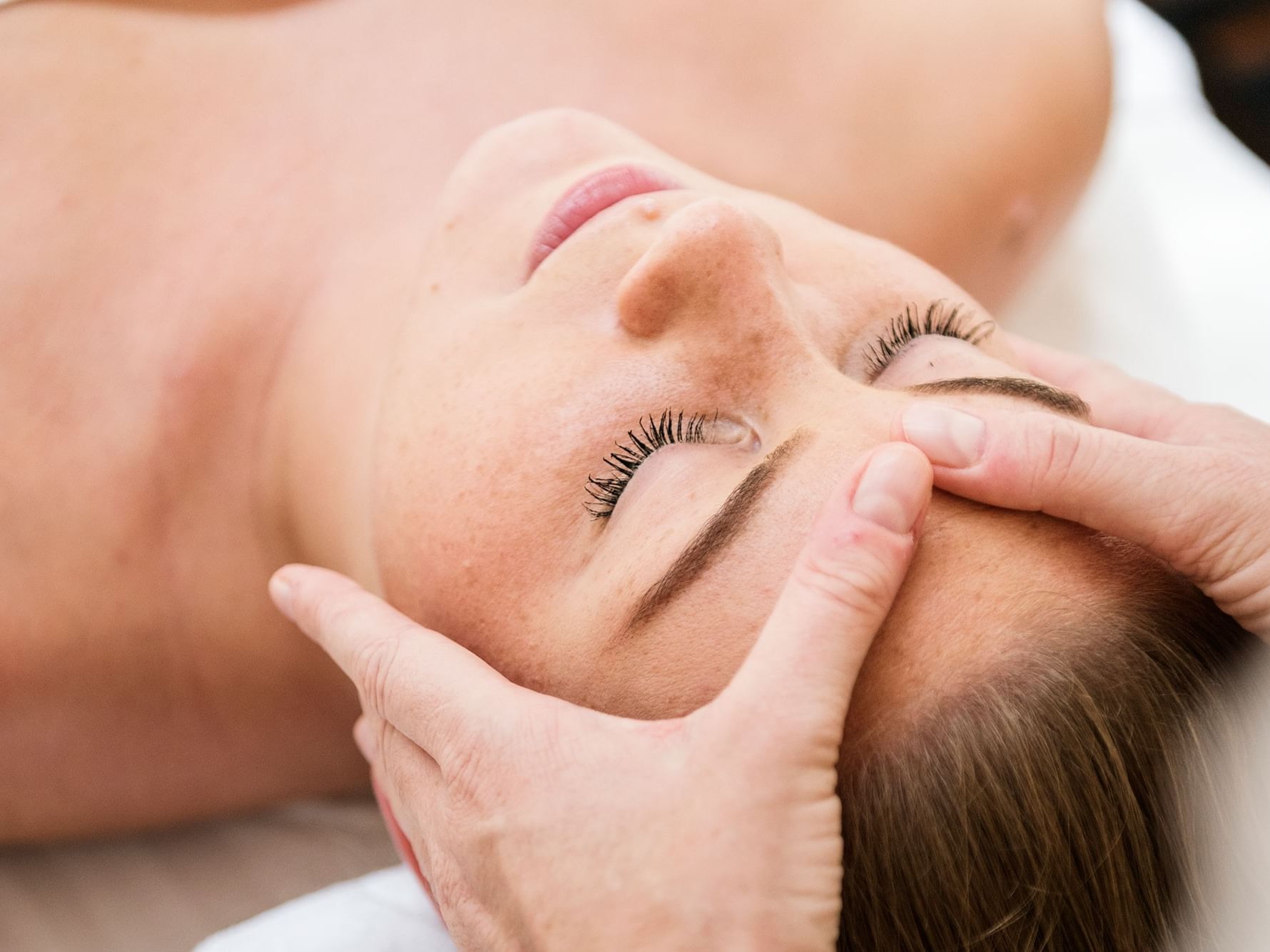A woman lying down receiving a facial massage on her forehead and cheeks.