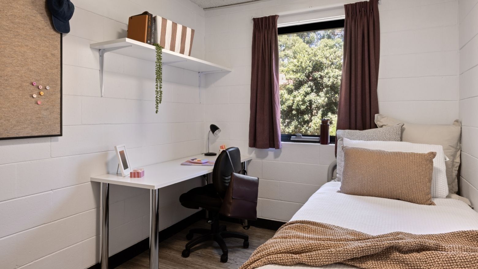 Cozy room with desk, bed, and window view of trees at UniLodge Guild House.