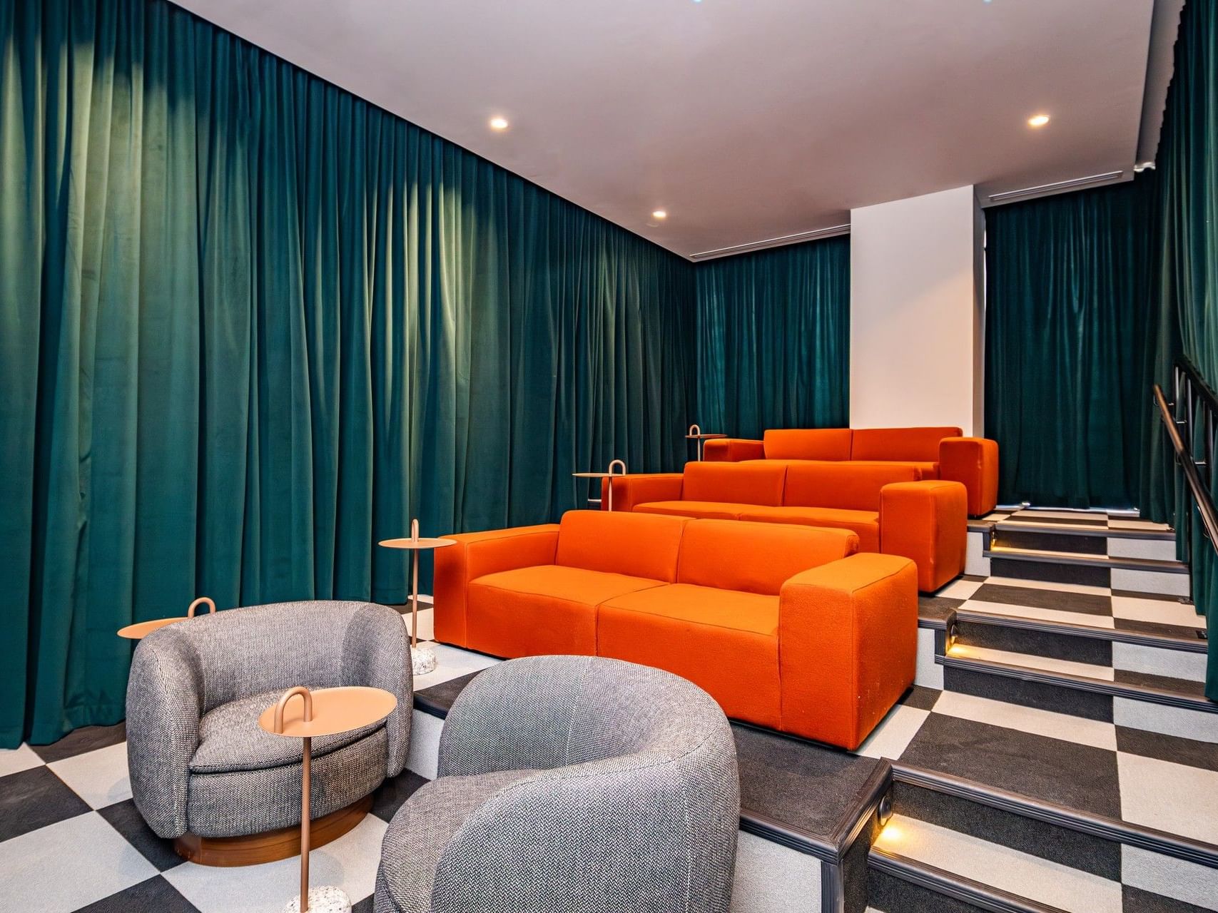 Modern Movie Lounge theater with tiered orange sofas, gray armchairs, & teal velvet curtains at The Crosby Miami World Center