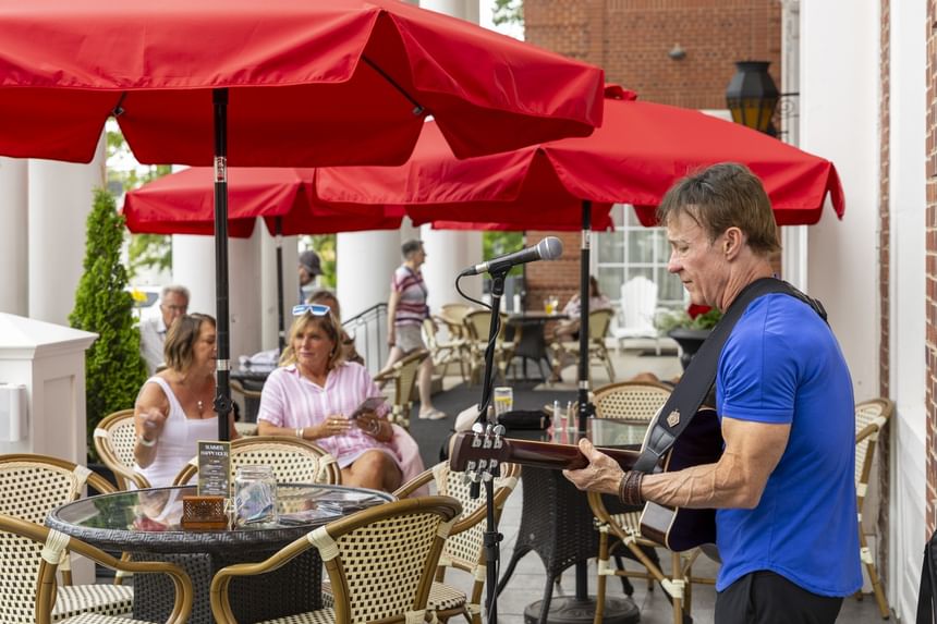 Musician sings into a microphone by a patio table under large red umbrellas at Rodd Charlottetown Hotel