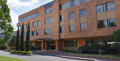 The facade of Habitel Hotel Select in the daytime, with brick architecture and tall green trees lining the entrance