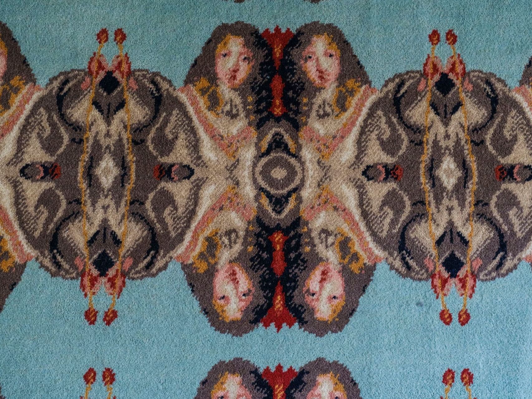 Blue rug with a symmetrical pattern of faces and red flower designs.