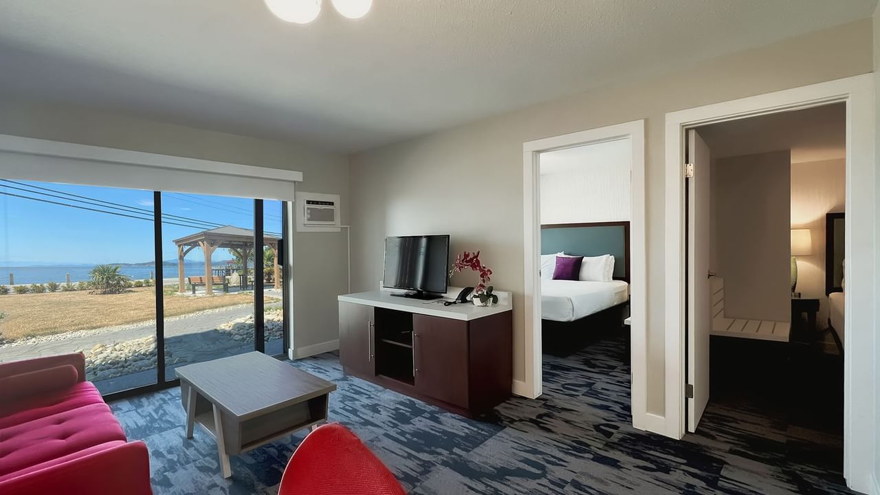 Guest room living area with red couch, coffee table, tv, patio doors, ocean view and patio with red deck chairs