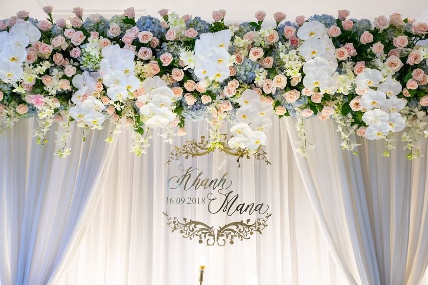 Floral arrangement featuring white orchids and pink roses above a sign with names and date at Park Hyatt Saigon