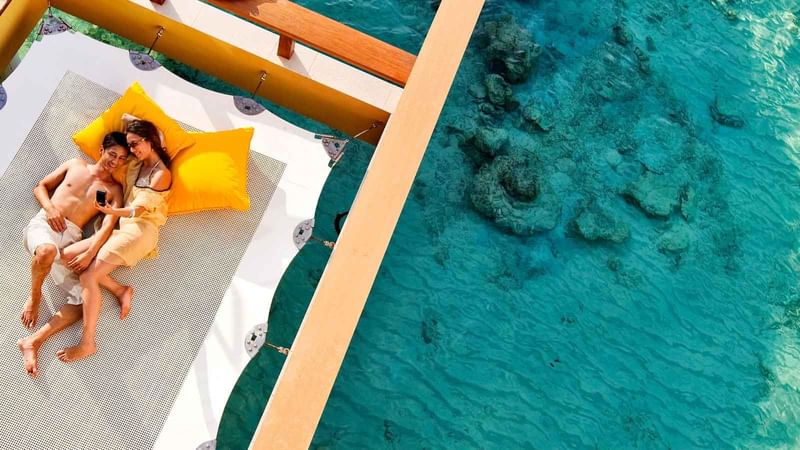 Aerial view of a couple lounging by clear blue ocean waters with coral underneath near Mercure Kooindah Waters