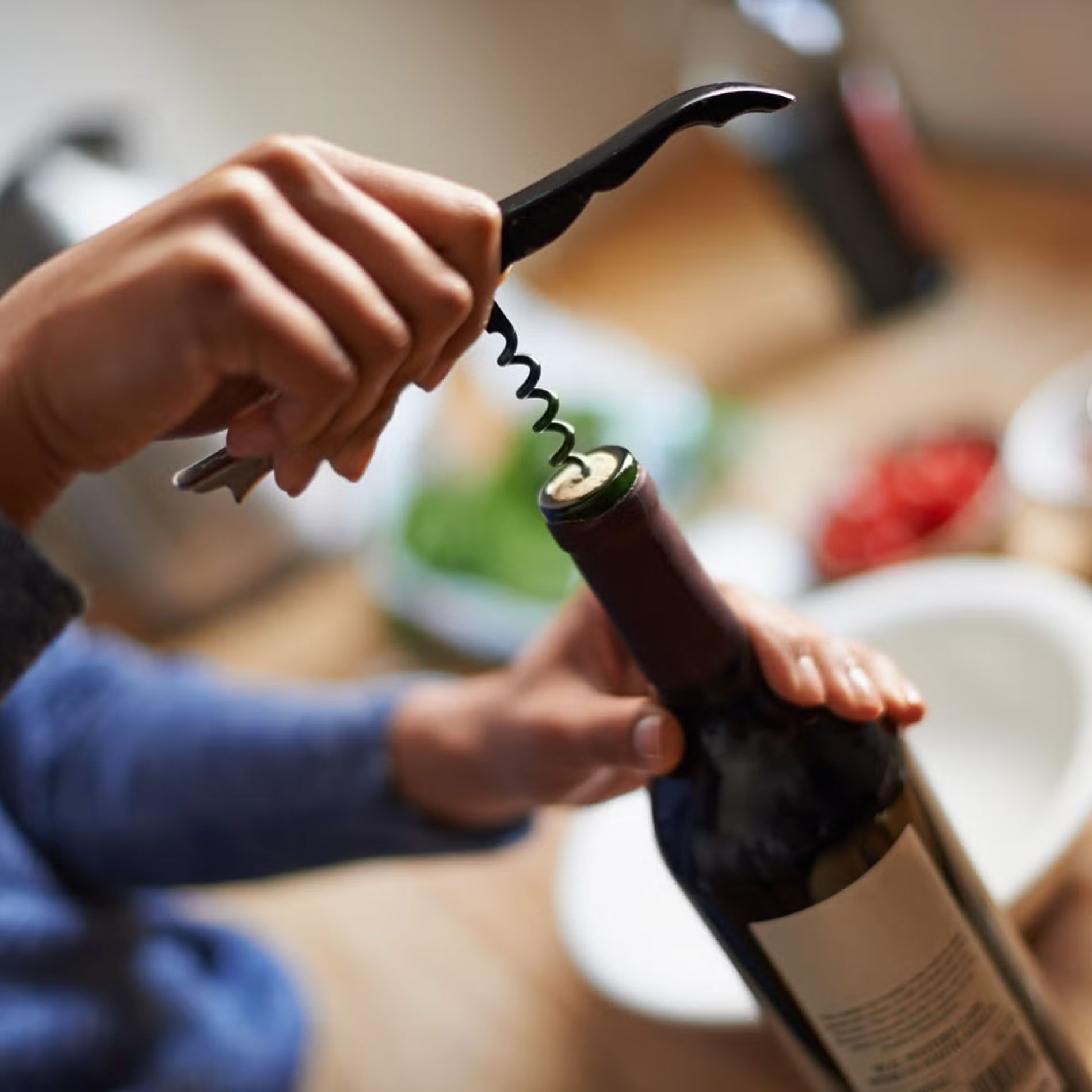 Close-up shot of hands using a corkscrew to open a bottle of red wine inside an apartment at Tradewinds Apartment Hotel