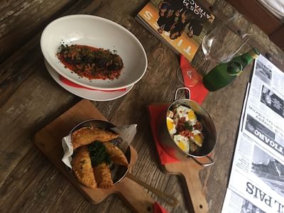 Top view of chorizo casserole, appetizers, wine, and magazine on rustic table at Billini Hotel Historic Luxury