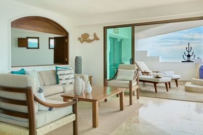 Living room with couch, chairs, table, sliding glass doors, and view of outdoor lounge with ocean backdrop.