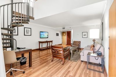 Spacious living area with sofa and wooden armchairs near a spiral staircase and desk in Lanai Suite at Miami Lakes Hotel