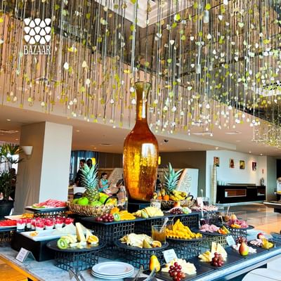 Fruit buffet with pineapple, melon, & assorted desserts beneath hanging decor in Bazaar at Megapolis Hotel Panama