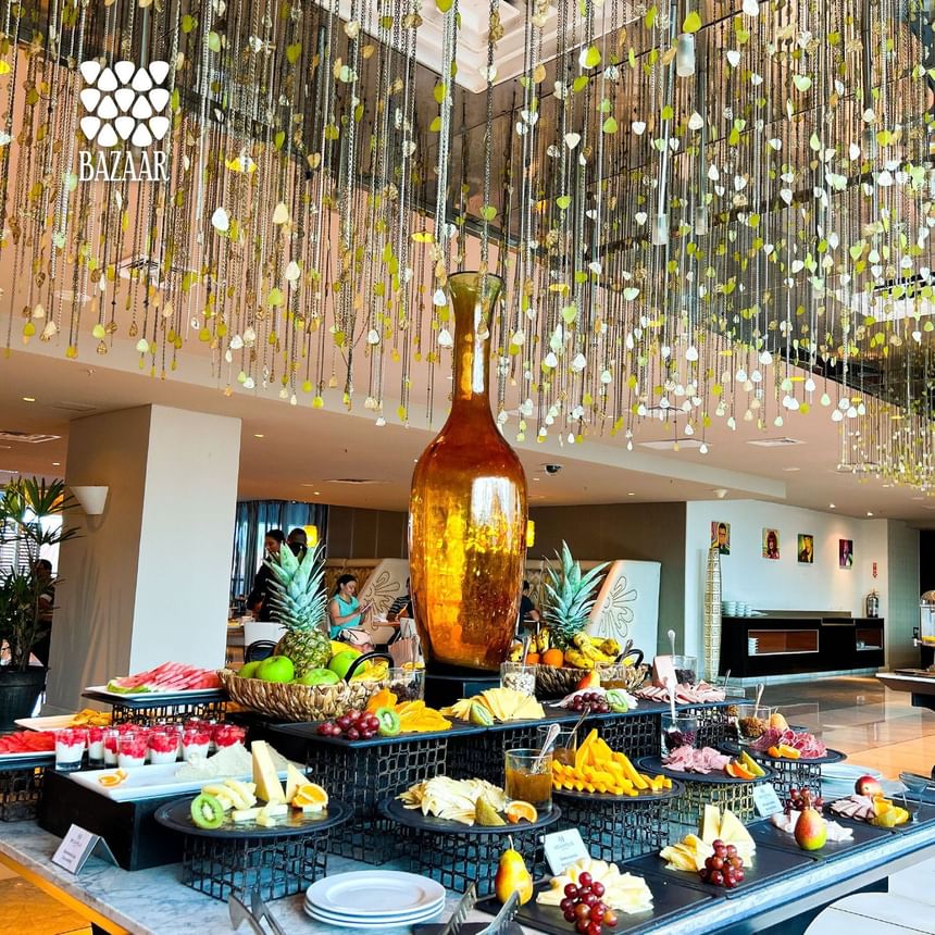 Fruit buffet with pineapple, melon, & assorted desserts beneath hanging decor in Bazaar at Megapolis Hotel Panama