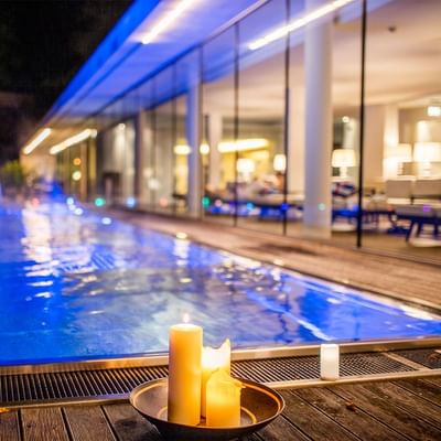 Nachtszene eines beleuchteten, modernen Swimmingpools mit Kerzen, umgeben von einer eleganten Glasfassade.