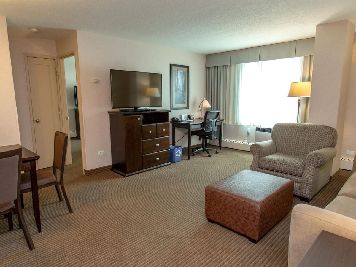 Hotel suite living area with a sofa, armchair, ottoman, dining table, TV and work desk.