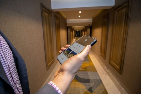 Persona con móvil que muestra la app Araiza Hotels en pasillo iluminado con puertas de habitaciones
