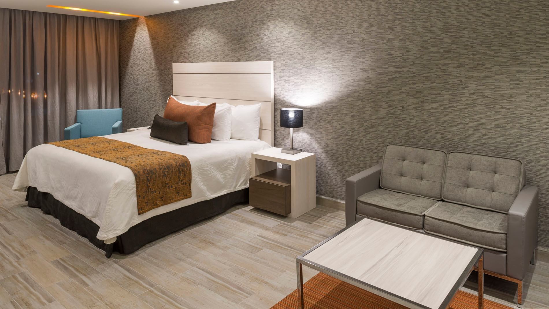 King Junior Suite with a textured grey accent wall, a soft grey sofa, and a white nightstand at Real Inn Celaya