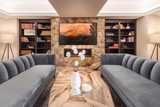 A living room at The Stanley Hotel with two grey couches, a stone fireplace, and built-in bookshelves with a TV