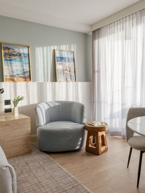 Sunset View Deluxe King at Elysium Manly featuring a marble table by a grey armchair under sunlit curtains near a bed