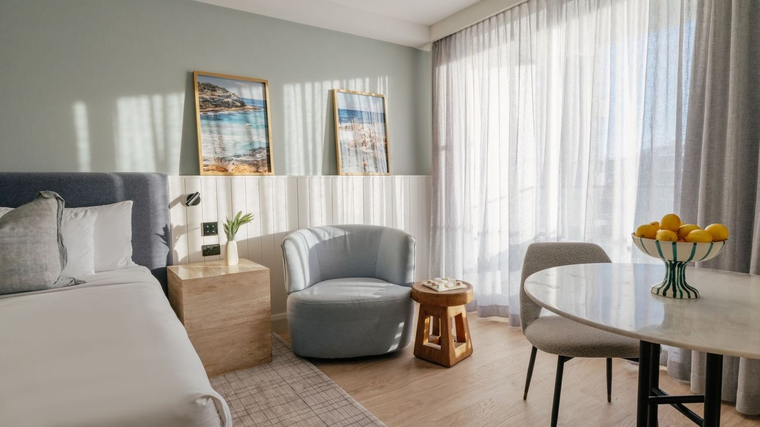 Sunset View Deluxe King at Elysium Manly featuring a marble table by a grey armchair under sunlit curtains near a bed