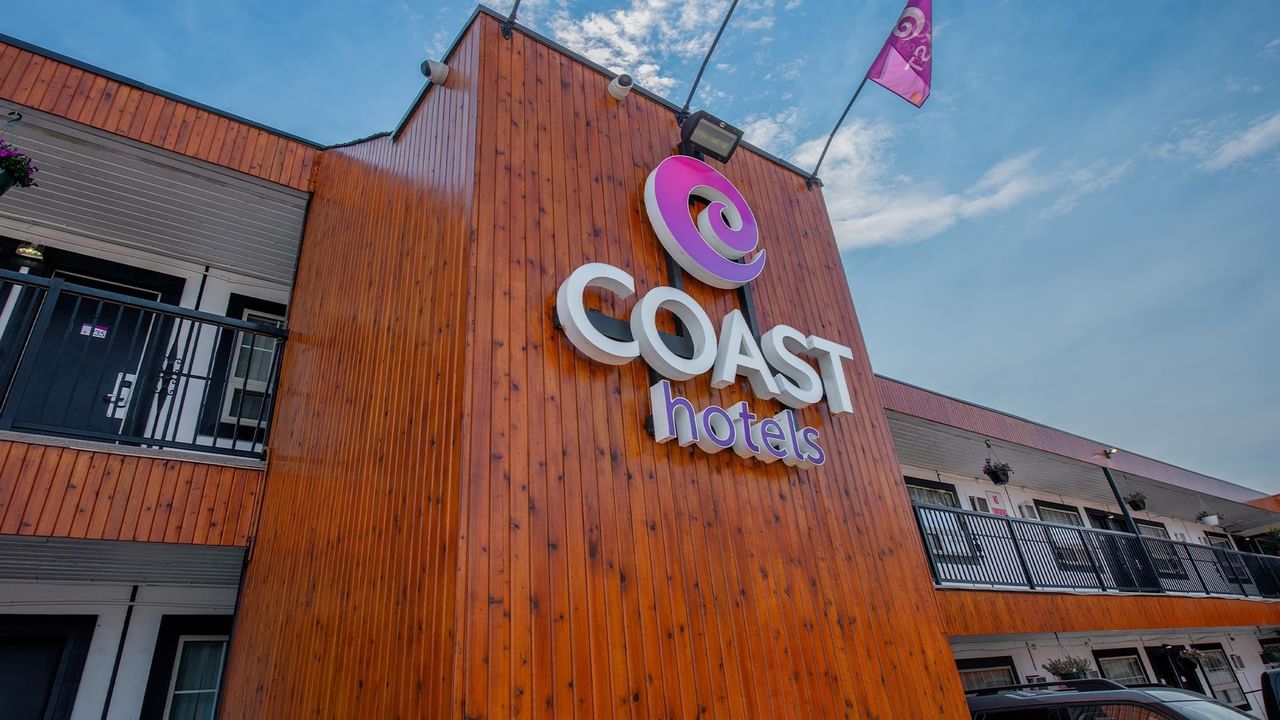 Close-up exterior view of the Coast Hotels sign mounted on the hotel building, with guest room balconies in the background.
