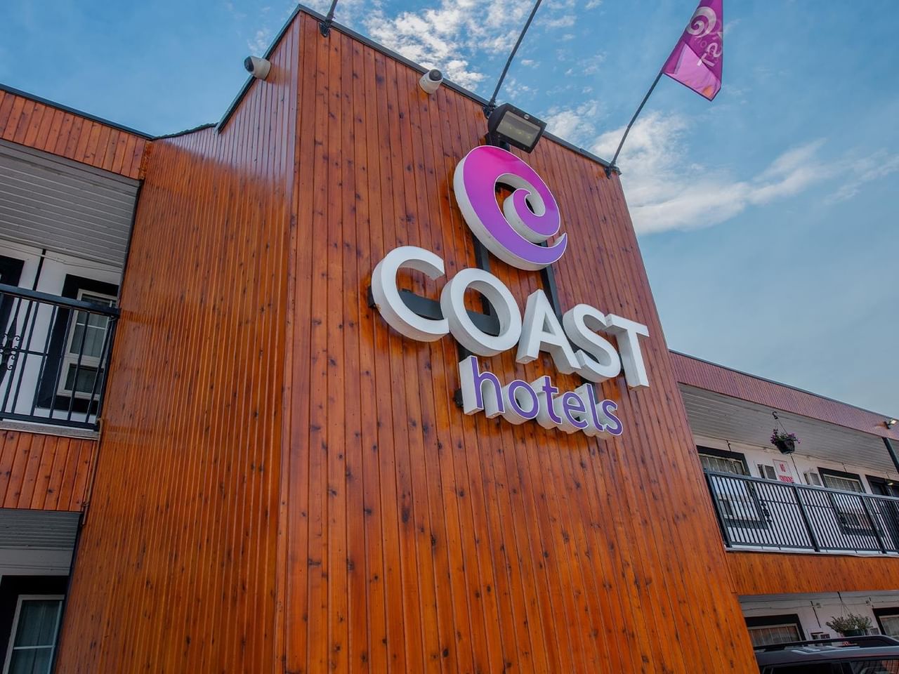 Close-up exterior view of the Coast Hotels sign mounted on the hotel building, with guest room balconies in the background.