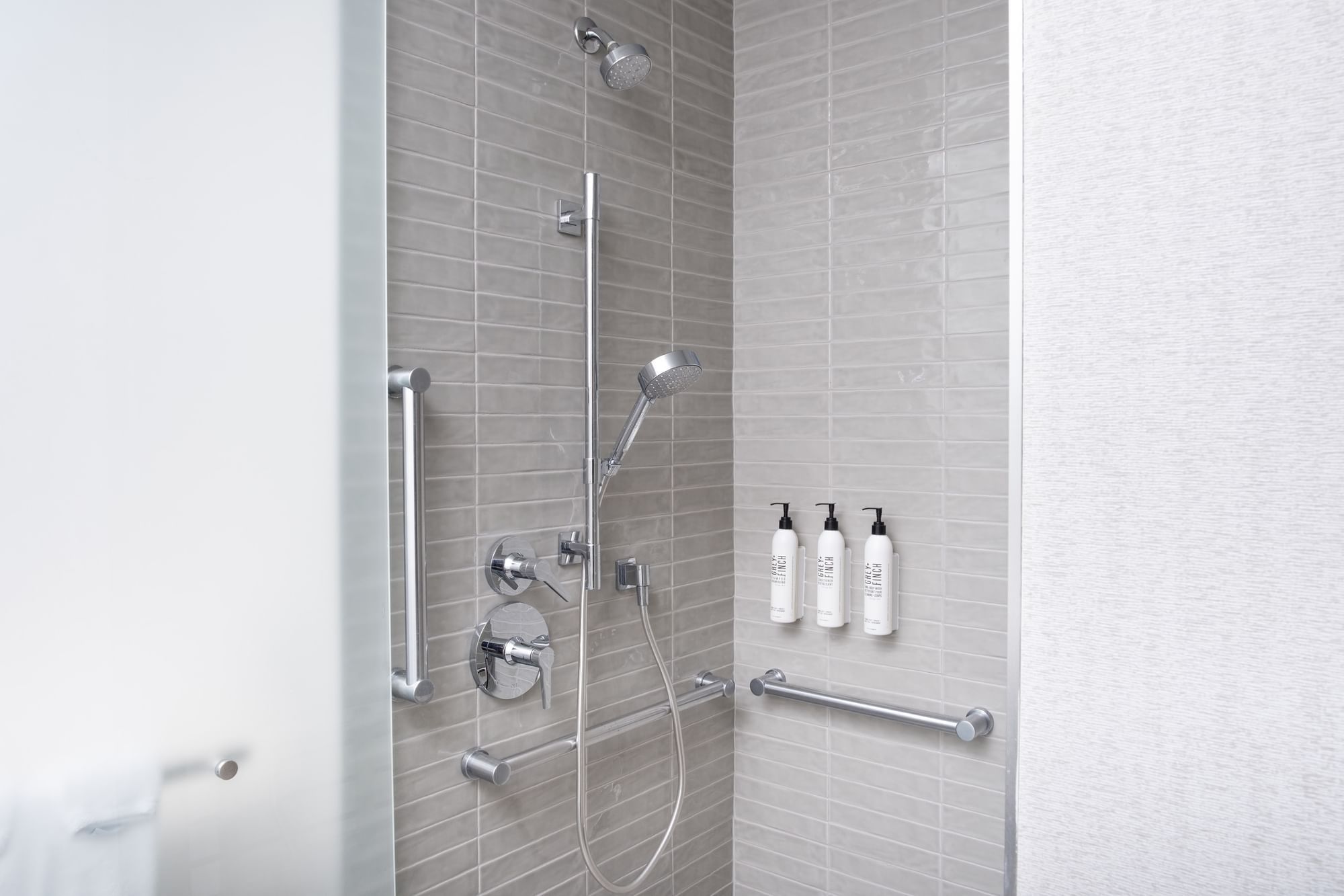 A modern shower with tiled walls, grab bars, a rain showerhead, and body sprays.