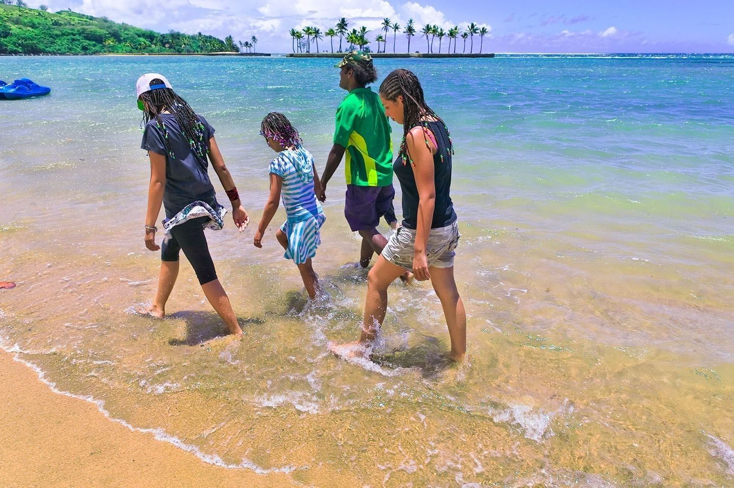 Family walking by the tide & a palm-lined islet under a blue summer sky near The Naviti Resort - Fiji