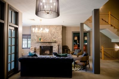 Plush dark sofa with armchairs facing a stone fireplace and wooden staircase at La Tourelle Hotel and Spa