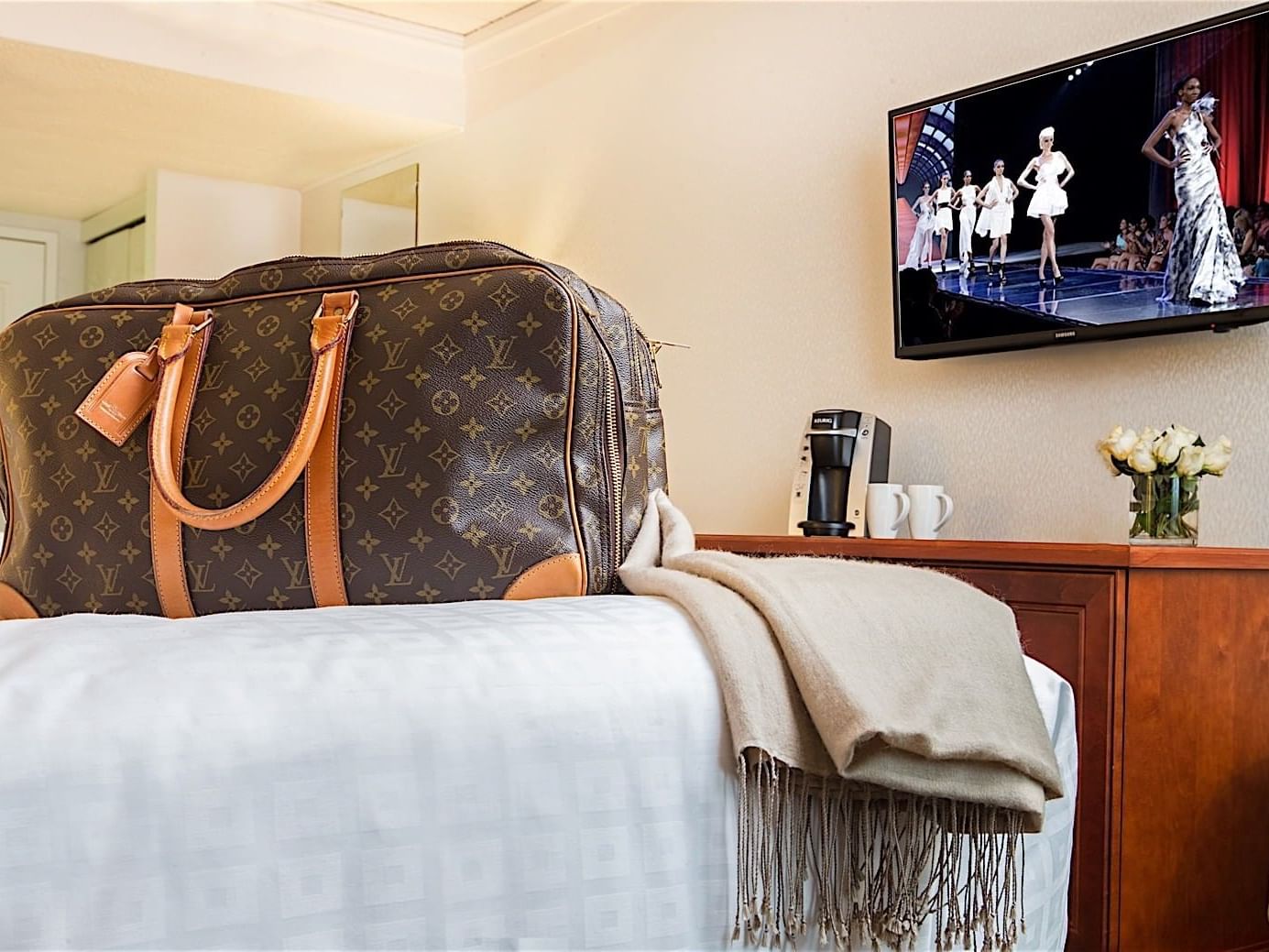 A bag tossed on a comfy bed with TV on at Metterra Hotel on Whyte