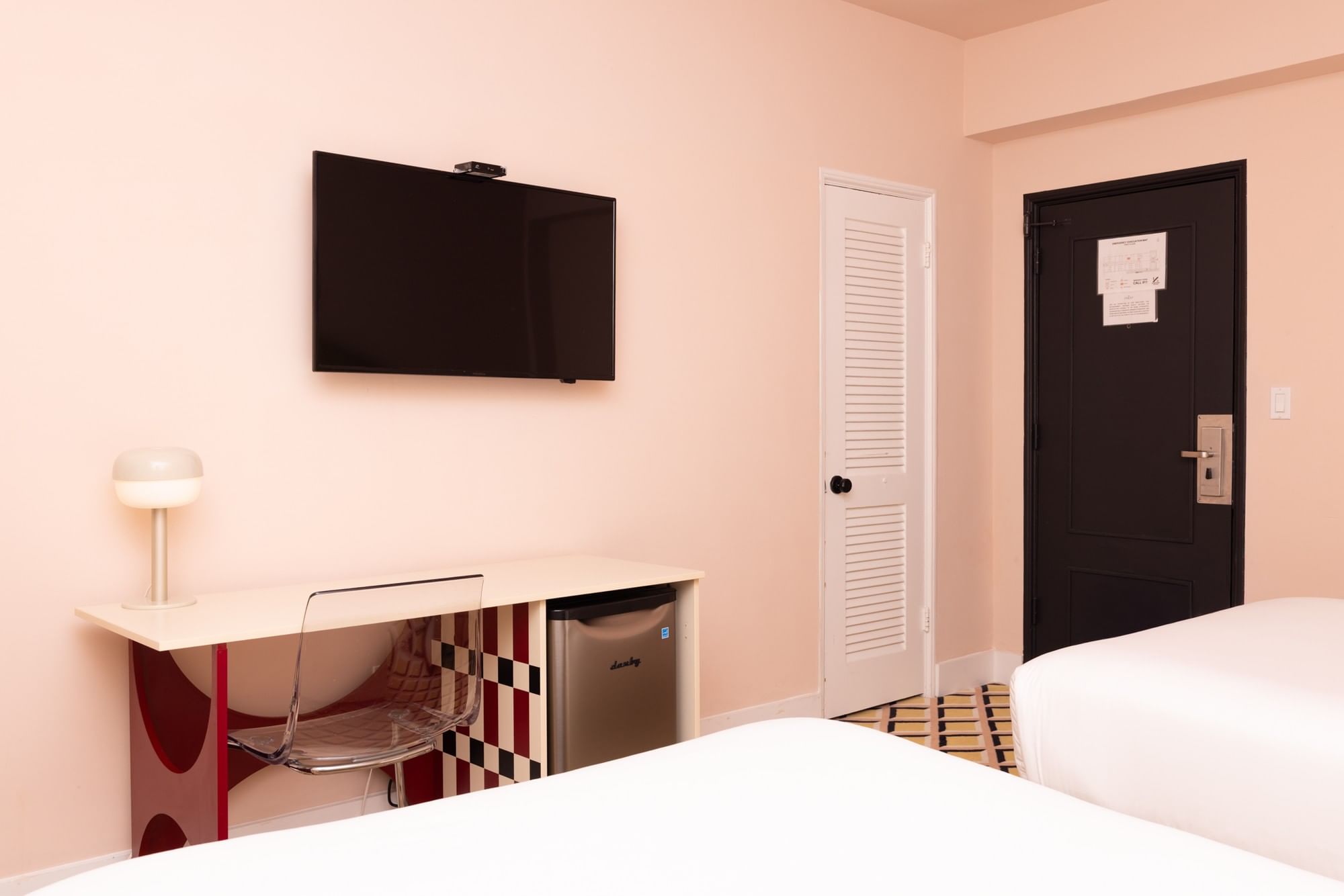 A hotel room with a double bed, desk, TV, and mini-fridge.
