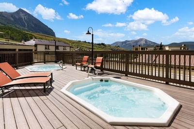Two hot tubs and lounge chairs on a wooden deck with a mountain view at Elevation Resort and Spa