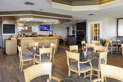Restaurant dining area featuring wooden tables and chairs by a large bar counter at Rodd Brudenell River Resort