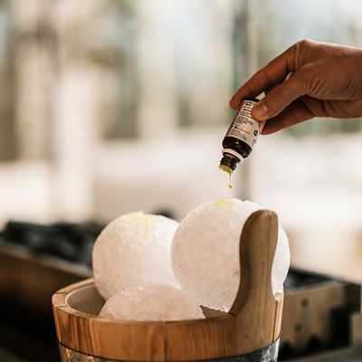 Eine Hand gießt Öl auf drei Seifenkugeln in einem Holzeimer.
