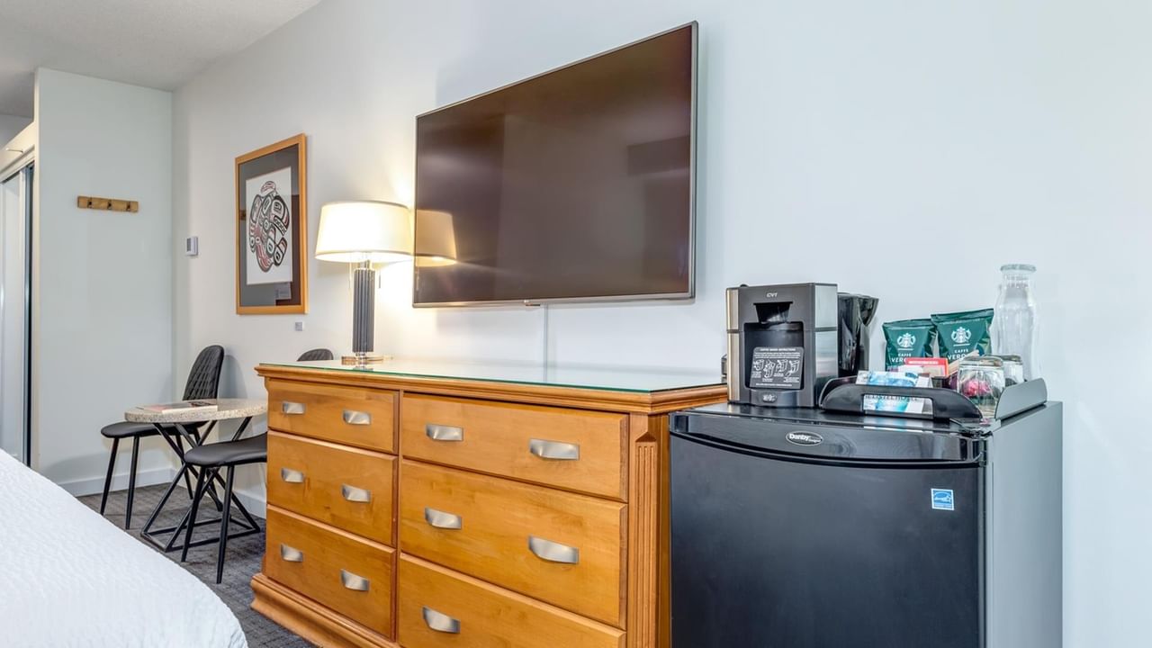 A hotel room with a bed, dresser, refrigerator, coffee maker, and TV on the wall.