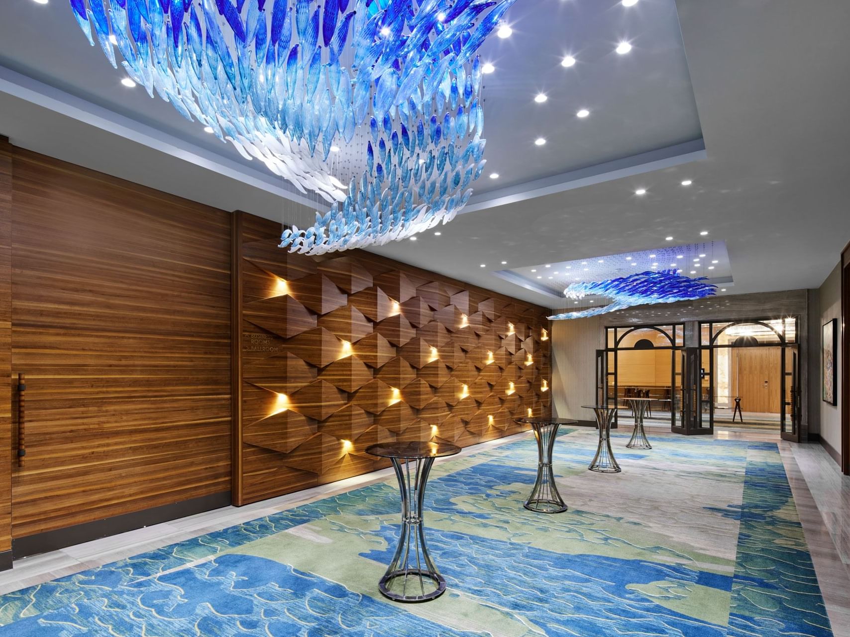 Großer Korridor mit blauen Wandteppichen, Kronleuchtern und geometrischen Holzwänden – Titanic Chaussee Berlin.