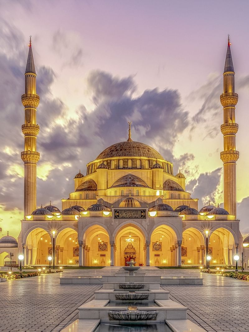 Illuminated Kocatepe Mosque with ornate architecture and surrounding landscape at dusk.